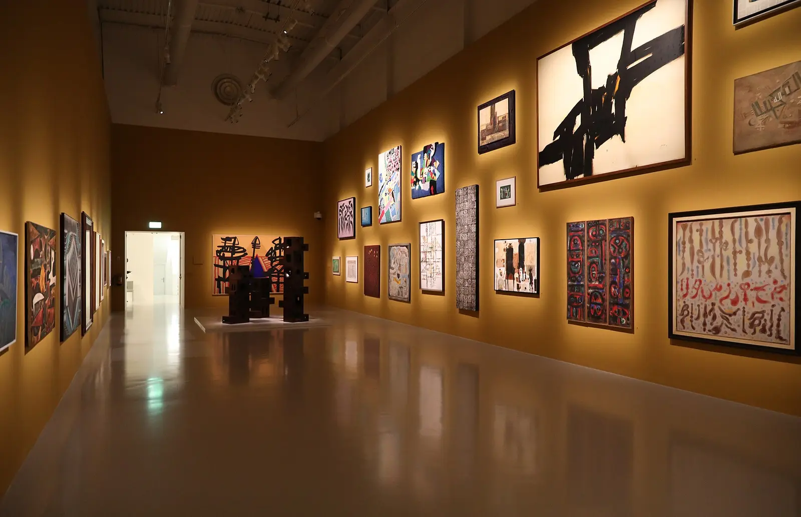 Warmly lit gallery hall hung with modern Arab paintings at Mathaf